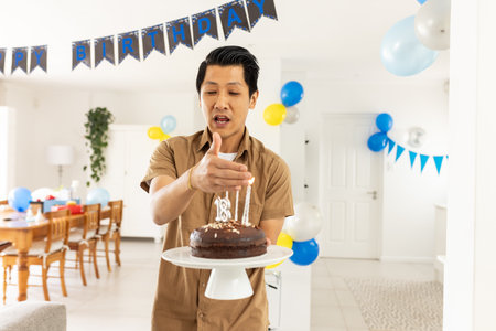 Man carrying birthday cake with lit candles in decorated living room. Celebration, party, festive, joyful, dessert, decorationの写真素材