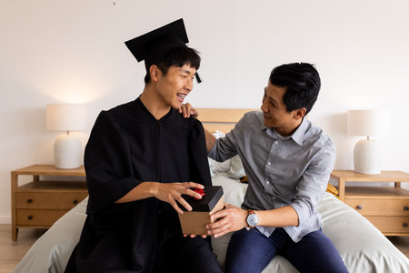 Graduation celebration, father congratulating son in cap and gown at home. achievement, proud, happiness, accomplishment, family, parentingの写真素材