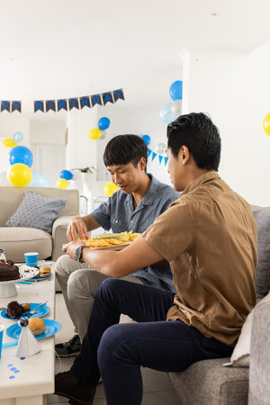 Celebrating at home, two men enjoying snacks at festive birthday party. Celebration, friendship, foodの写真素材