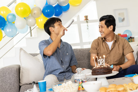 Celebrating birthday, two men enjoying cake and laughter in festive living room. Celebration, party, happiness, friendship, dessert, gatheringの写真素材