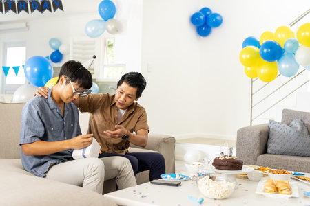 Father and son celebrating birthday at home, opening gifts with joy. Family, celebration, happiness, fatherhood, presents, togethernessの写真素材