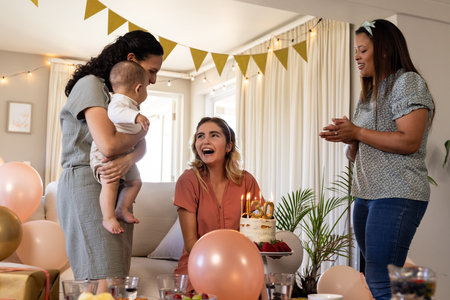 Celebrating birthday, woman holding cake with friends and baby in living room. Celebration, party, family, happiness, gathering, togethernessの写真素材