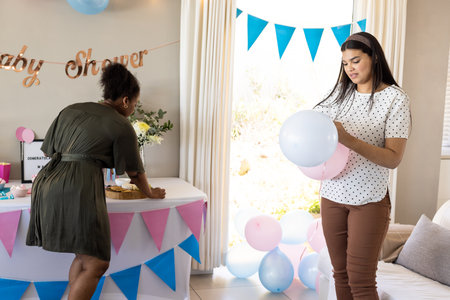 Decorating for baby shower, women preparing balloons and arranging table indoors. Celebration, party, decorations, preparation, festive, gatheringの写真素材