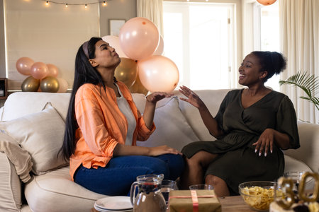 Women laughing and enjoying conversation on sofa during festive home gathering. Celebration, friendship, togetherness, bonding, happiness, lifestyleの写真素材