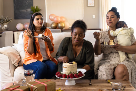 African American women enjoying cake and celebrating at home with baby. Celebration, family, happiness, motherhood, parenting, relaxationの写真素材
