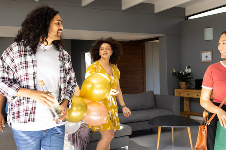 Friends celebrating at home, holding balloons and bottle, enjoying festive gathering. Celebration, party, happiness, togetherness, cheerful, joyfulの写真素材