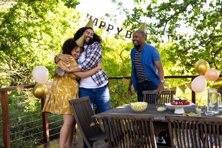 African American friends celebrating birthday outdoors, hugging and laughing with party hats. Celebration, friendship, diversity, happiness, festivities, joyの写真素材