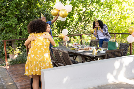 Celebrating birthday outdoors, friends with balloons and party hats sharing hugs. Celebration, friendship, gathering, joy, happiness, festivityの写真素材