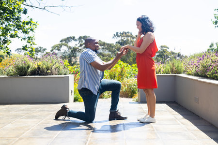 Man proposing to woman on sunny terrace, both smiling and feeling joyful. Engagement, romance, happiness, relationship, outdoor, proposalの写真素材