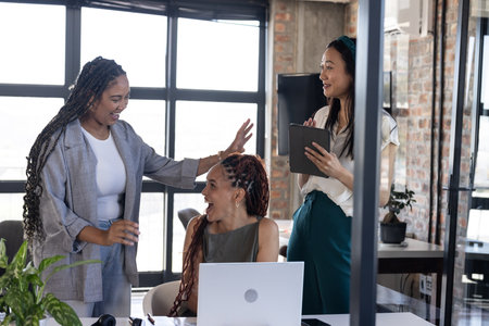 Colleagues celebrating success at office with laptop and digital tablet. Teamwork, business, collaboration, celebration, technology, meetingの写真素材