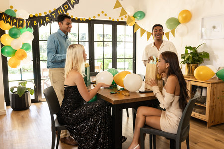 Friends celebrating birthday at home, smiling and exchanging gifts with balloons. Celebration,...