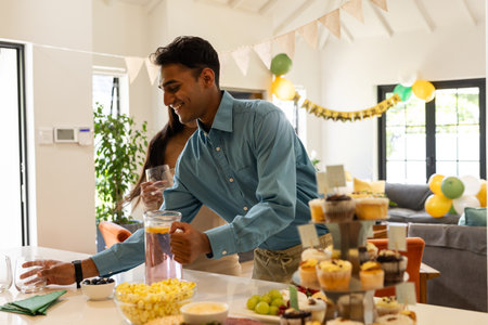 Man serving drinks at home party with cupcakes and festive decorations. Celebration, hospitality,...
