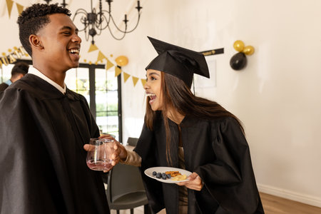 Graduates in caps and gowns celebrating with snacks and drinks at party. Graduation, celebration, university, achievement, alumni, friendsの写真素材