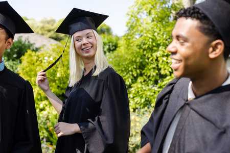 Graduating students in caps and gowns celebrating outdoors, smiling and chatting. Graduation, ceremony, joy, achievement, friends, excitementの写真素材