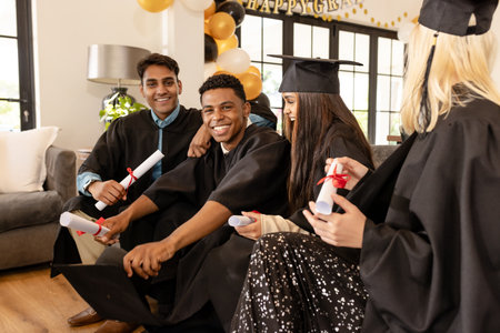 Graduates in caps and gowns celebrating success with diplomas at home. Graduation, achievement, celebration, academic, higher education, ceremonyの写真素材