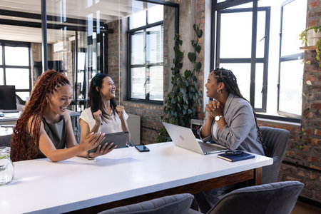 Diverse business team celebrating success with laptops and tablets in modern office. Corporate, teamwork, technology, collaboration, celebration, diversityの写真素材