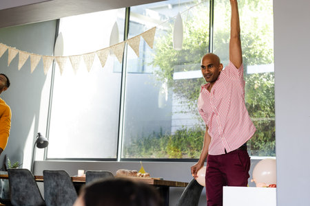 Man in striped shirt raising hand at home celebration, looking cheerful. casual, joy, hand gesture, happiness, domestic, social gatheringの写真素材