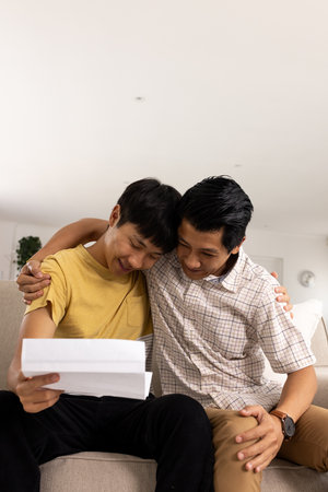 Father and son celebrating good news together while reading letter on couch. Family, happiness, bonding, living room, mail, joyの写真素材