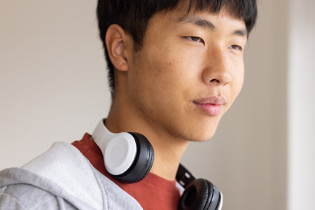 Young man with headphones around neck looking thoughtfully, wearing casual hoodie. contemplation, fashion, tech, lifestyleの写真素材