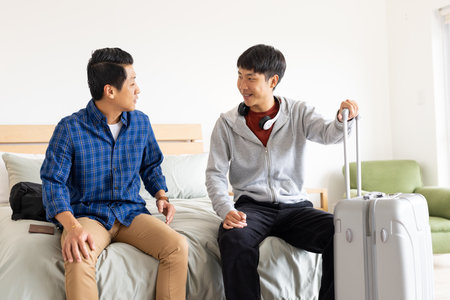 Friends talking and preparing for travel with suitcase in modern bedroom. vacation, friendship, packing, luggage, planning, tourismの写真素材