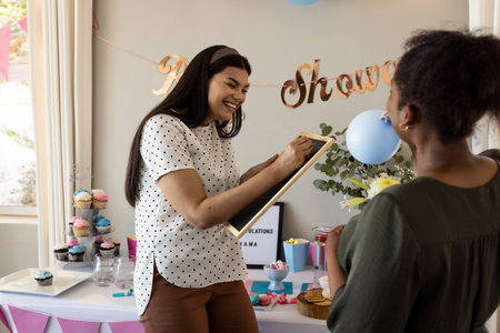 Smiling woman writing on clipboard at baby shower celebration with friends. joy, friendship, party, togetherness, maternity, happinessの写真素材