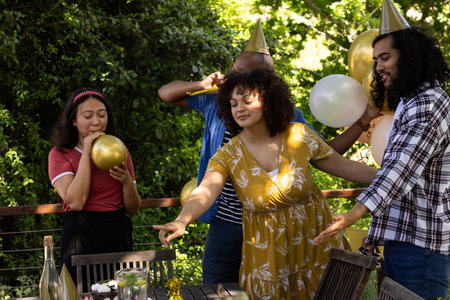 Friends celebrating outdoors, blowing balloons and wearing party hats with joy. Celebration, festivity, friendship, fun, happiness, cheerfulの写真素材