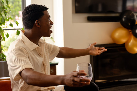 Man joyfully celebrating at home, holding glass, with festive balloons nearby. Celebration, party, happiness, toast, cheerfulの写真素材