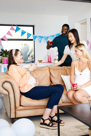 Friends celebrating at home, enjoying drinks and laughter on cozy sofa. Party, celebration, friendship, gathering, leisure, enjoymentの写真素材