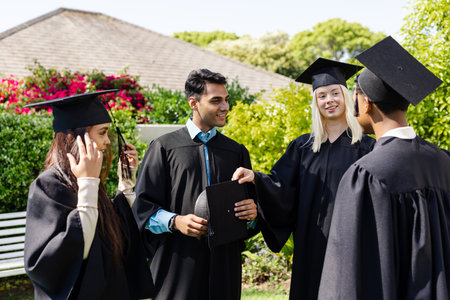 Graduates in caps and gowns celebrating together outdoors, smiling and talking. Graduation, celebration, academic, success, achievement, universityの写真素材