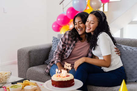 Celebrating birthday, two women hugging on couch with cake and balloons. Celebration, party, friendship, happiness, joy, togethernessの写真素材