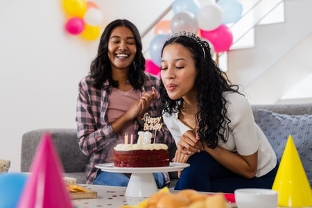 Celebrating birthday, young woman blowing candles on cake with friend clapping. celebration, party, friendship, happiness, enjoyment, festivityの写真素材