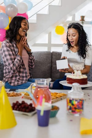 Exchanging gifts and eating cake, African American women celebrating birthday at home. Celebration, party, gift-giving, friendship, happiness, dessertの写真素材