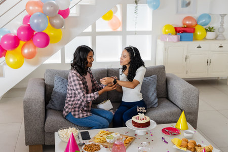 Celebrating birthday, two women exchanging gifts on sofa with cake and snacks. Celebration, friendship, presents, party, happiness, cheerfulの写真素材