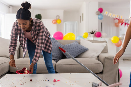 Cleaning up after party, woman tidying living room with balloons and confetti. Housekeeping, party cleanup, organizing, domestic, celebration, choresの写真素材
