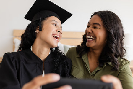 Graduation day, mother and daughter laughing and taking selfie at home. Celebration, family, happiness, bonding, diploma, achievementの写真素材