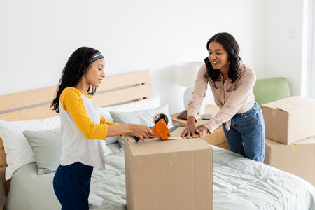 Mother and daughter packing cardboard box together on bed, smiling and bonding. Family, moving, relationship, happiness, home, activityの写真素材