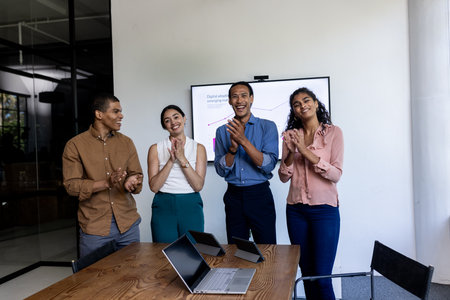 In office, team applauding successful business presentation with laptops on table. Teamwork, collaboration, achievement, applause, meeting, corporate