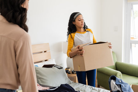 Woman carrying cardboard box in bedroom while organizing and tidying up space. Moving, unpacking, clean, home, lifestyle, relocationの写真素材