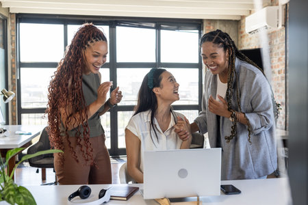 Colleagues celebrating success at office, smiling and cheering around laptop. Teamwork, collaboration, achievement, business, corporate, celebrationの写真素材