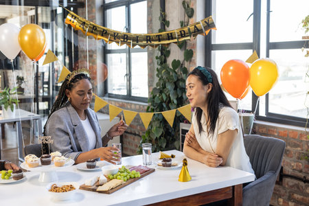 Celebrating birthday at office, two women enjoying snacks and conversation. celebration, colleagues, workplace, friendship, eventの写真素材