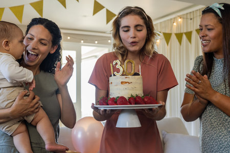 Blowing out candles, woman celebrating 30th birthday with friends and family. Celebration, milestone, friendship, happiness, party, cakeの写真素材