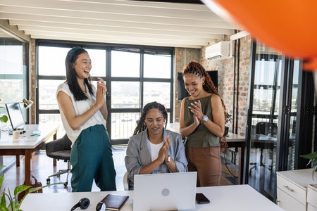 Colleagues celebrating success around laptop in modern office, clapping and smiling. Teamwork, victory, achievement, collaboration, business, workplaceの写真素材