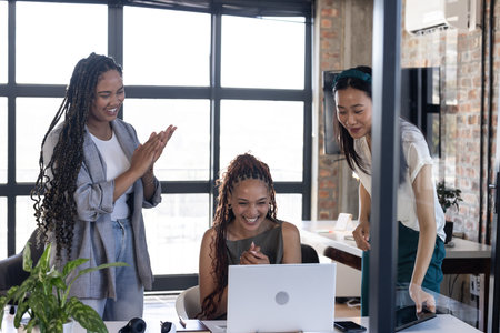 Colleagues celebrating success, smiling and clapping around laptop in modern office. Teamwork, collaboration, achievement, business, celebration, projectの写真素材