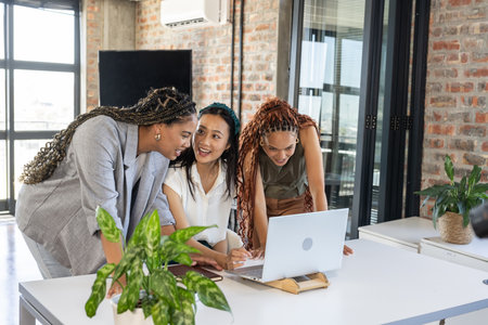 Colleagues collaborating around laptop in modern office, sharing ideas and smiling. Collaboration, teamwork, business, brainstorming, technology, communicationの写真素材