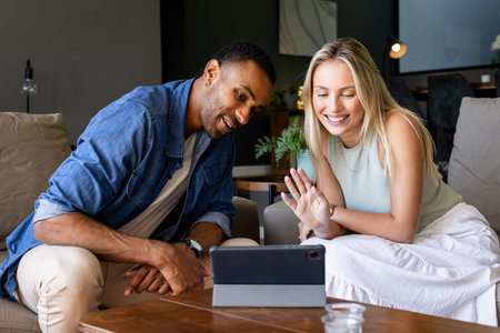 Smiling couple video chatting on tablet in cozy living room setting. Technology, communication, connectivity, bonding, leisure, happinessの写真素材