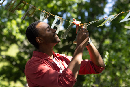 Man hanging birthday banner outdoors, smiling and enjoying sunny celebration. happiness, decoration, festive, cheerful, summertime, joyfulの写真素材