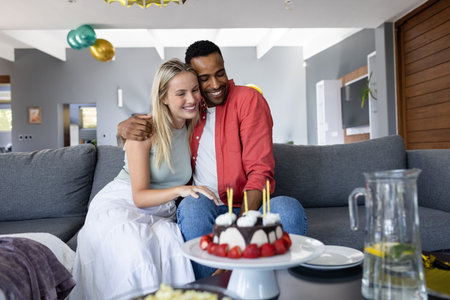 Couple celebrating birthday at home, smiling with cake and candles on table. Celebration, romantic, happiness, family, occasion, cheerfulの写真素材
