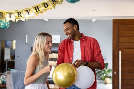 African American man and woman holding balloons, celebrating birthday indoors, smiling. Celebration, happiness, party, diverse, joyful, festiveの写真素材