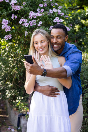In garden, smiling couple video calling on smartphone during outdoor celebration. communication, technology, outdoors, friendship, gathering, happinessの写真素材