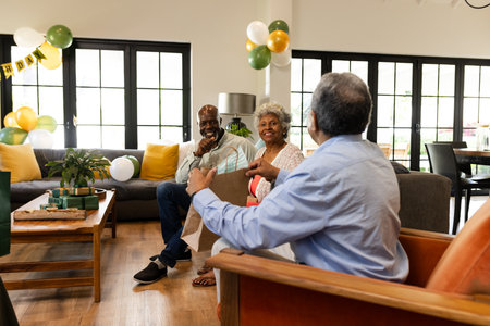Senior friends laughing and sharing gifts in cozy living room celebration. Friendship, storytelling, happiness, bonding, togetherness, laughterの写真素材